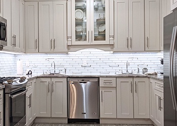A kitchen featuring light gray shaker cabinets and white tile backsplashes is illuminated by LED underpanel lights.