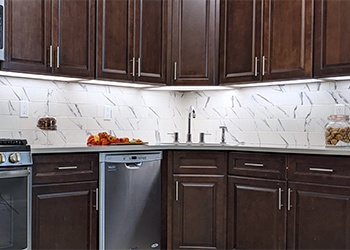 A dark brown wood texture kitchen is brightly illuminated by LED under-cabinet lighting.